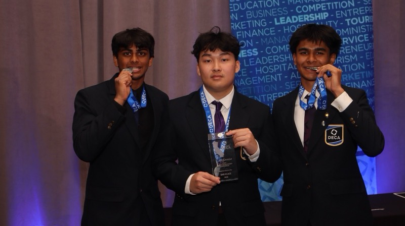 Three members showing their medals in front of the DECA backdrop