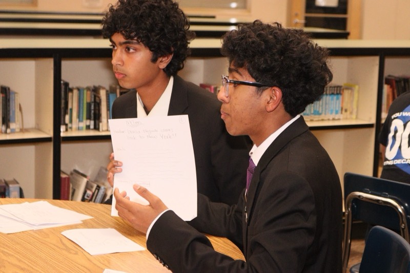 Two members practicing a roleplay across a table in the school library